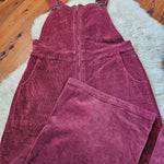 Maroon corduroy overalls on a wooden floor with a white rug.