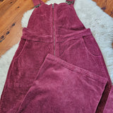 Maroon corduroy overalls on a wooden floor with a white rug.