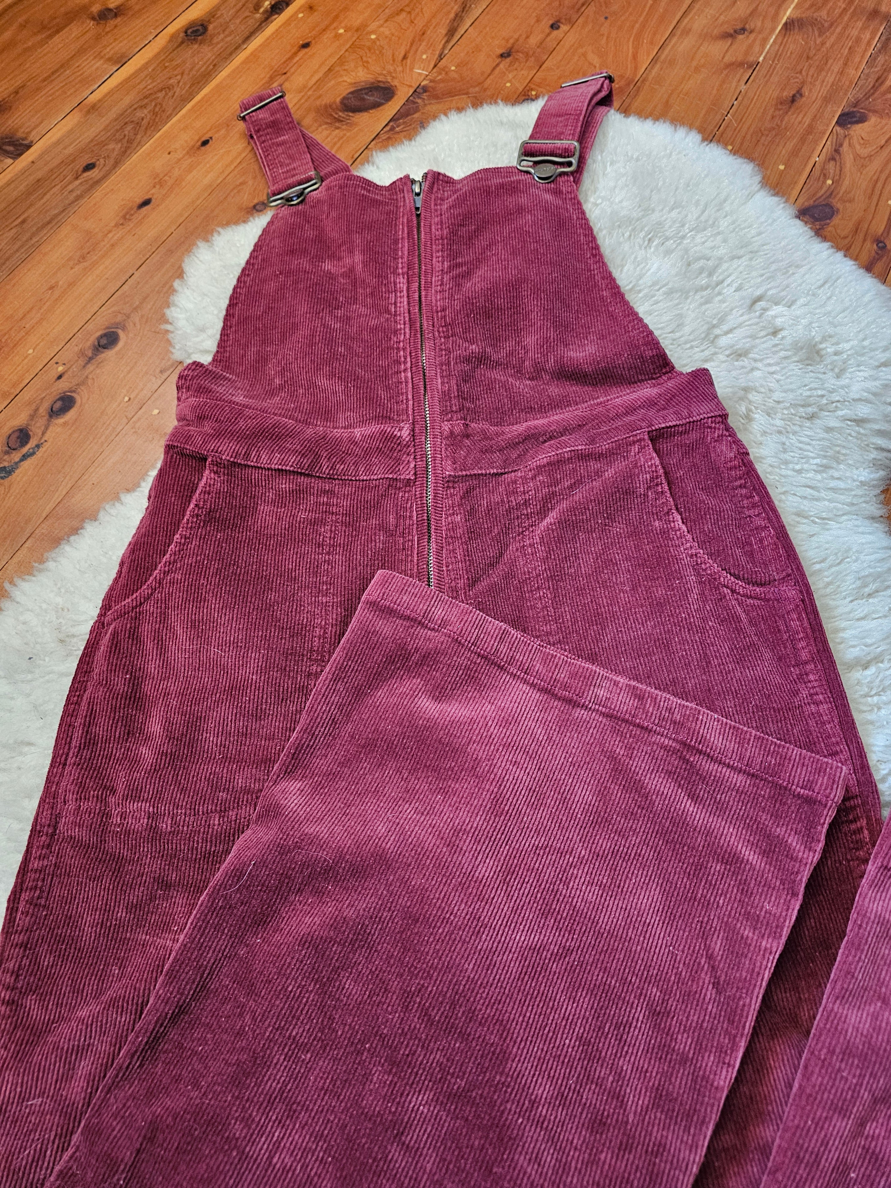 Maroon corduroy overalls on a wooden floor with a white rug.