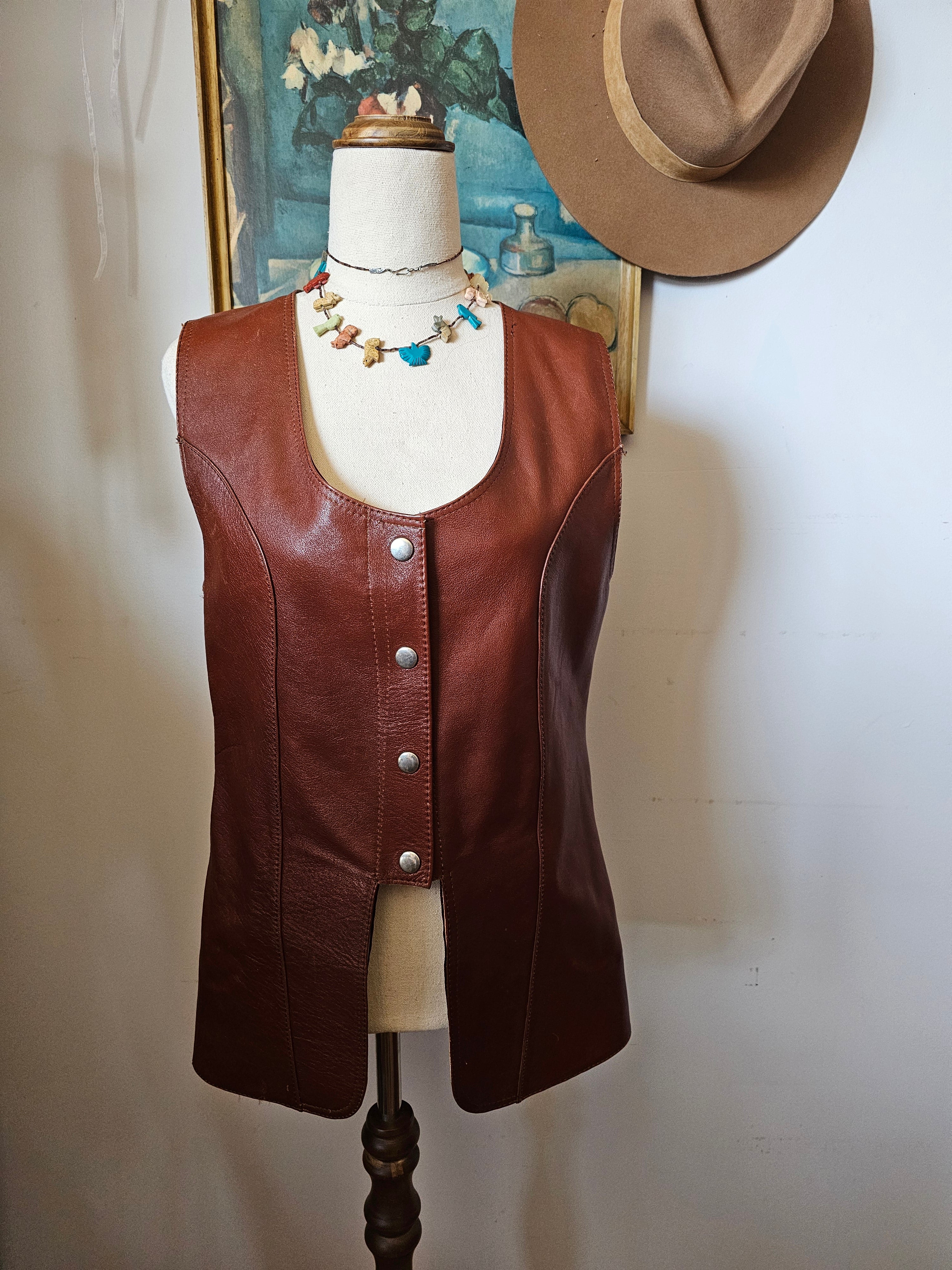 Brown leather saddle on a stand with a hat and decorative item in the background.