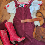 Red cowboy boots on a wooden floor with a saddle and horse blanket in the background.
