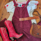 Red cowboy boots on a wooden floor with a saddle and horse blanket in the background.