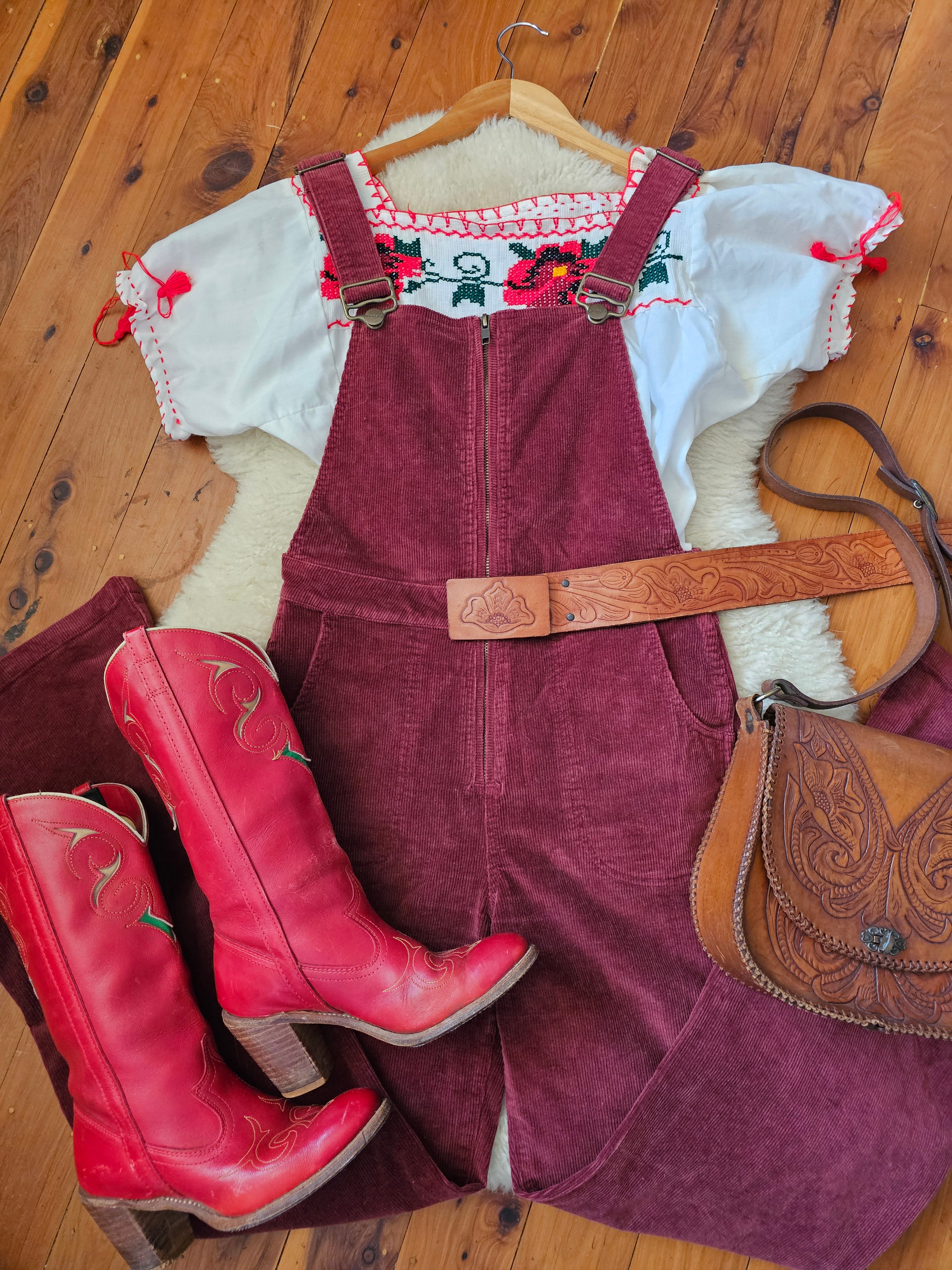 Red cowboy boots on a wooden floor with a saddle and horse blanket in the background.