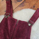 Maroon corduroy overalls with a strap on a wooden floor.