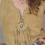 Person wearing a beige suede top with fringe details and a blue skirt with a decorative belt.