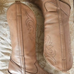Pair of brown leather boots with decorative stitching on a textured surface