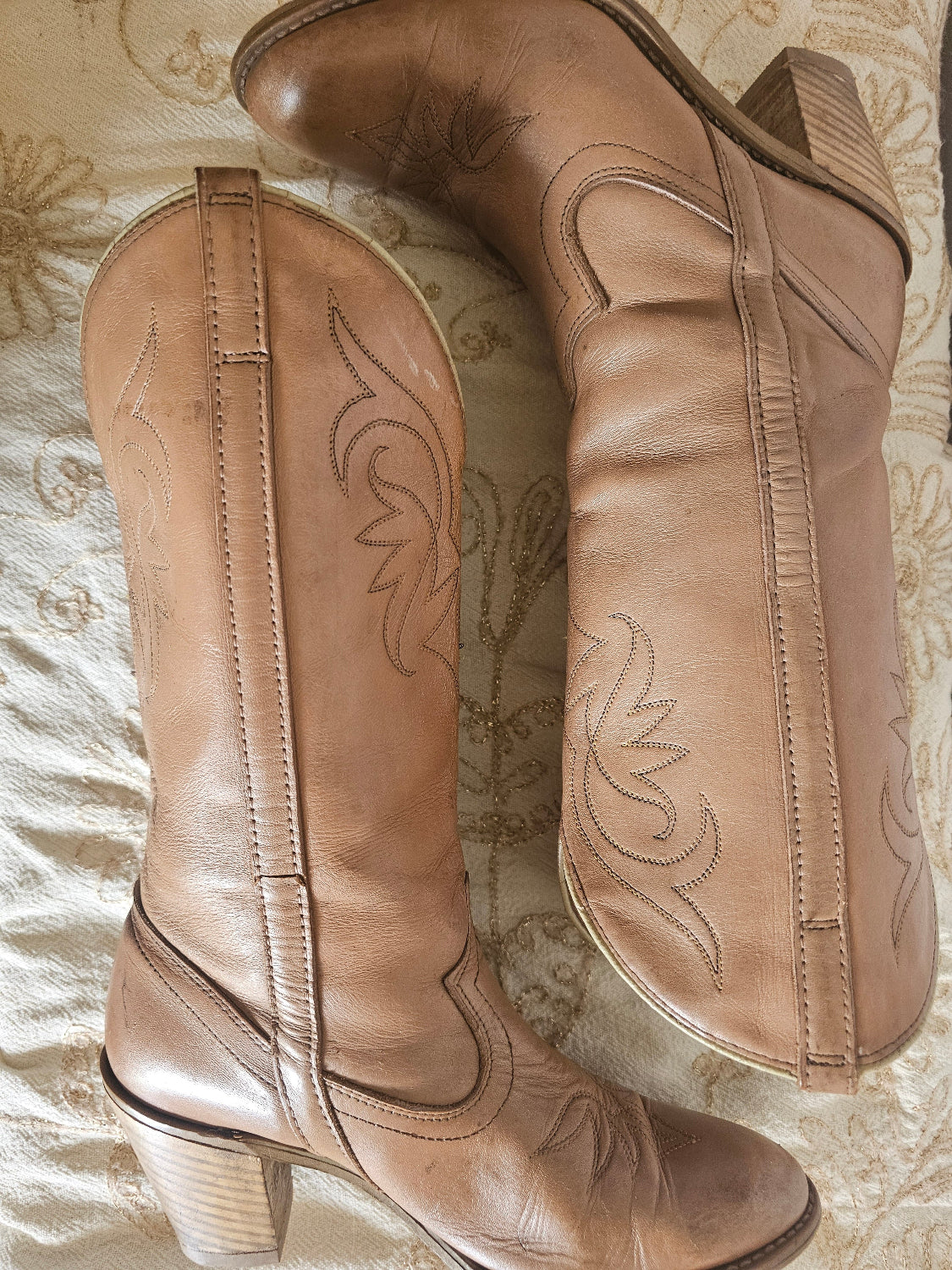 Pair of brown leather boots with decorative stitching on a textured surface