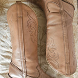 Pair of brown leather boots with decorative stitching on a textured surface