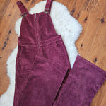 Maroon corduroy overalls on a wooden floor with a white rug underneath