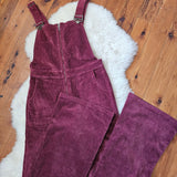 Maroon corduroy overalls on a wooden floor with a white rug underneath