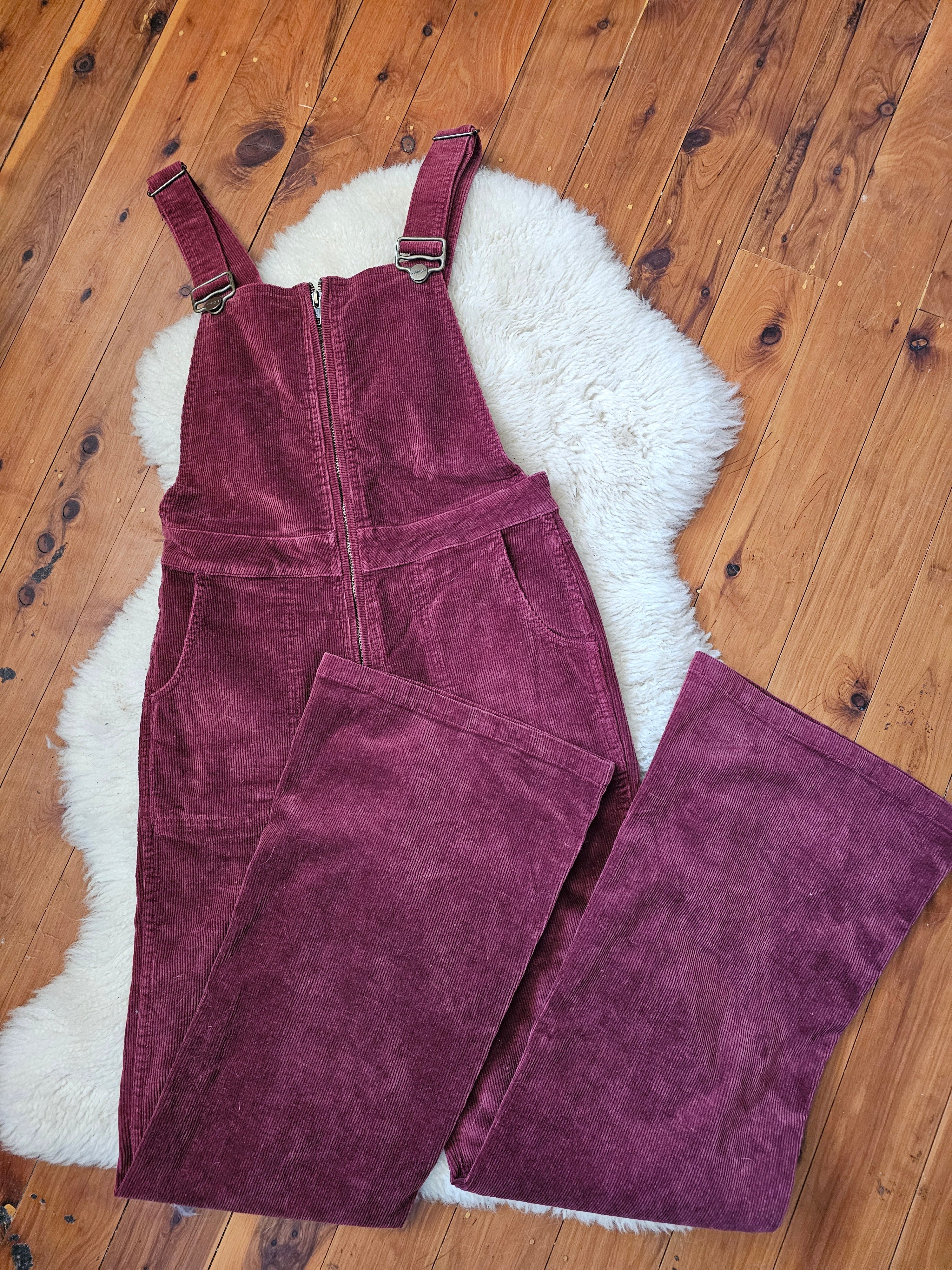 Maroon corduroy overalls on a wooden floor with a white rug underneath