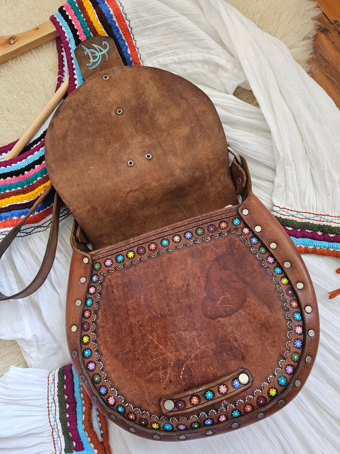 Brown leather saddle with colorful studs on a white background