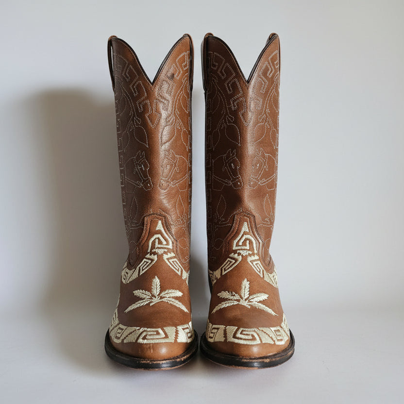 Pair of brown cowboy boots with white patterns on a light background