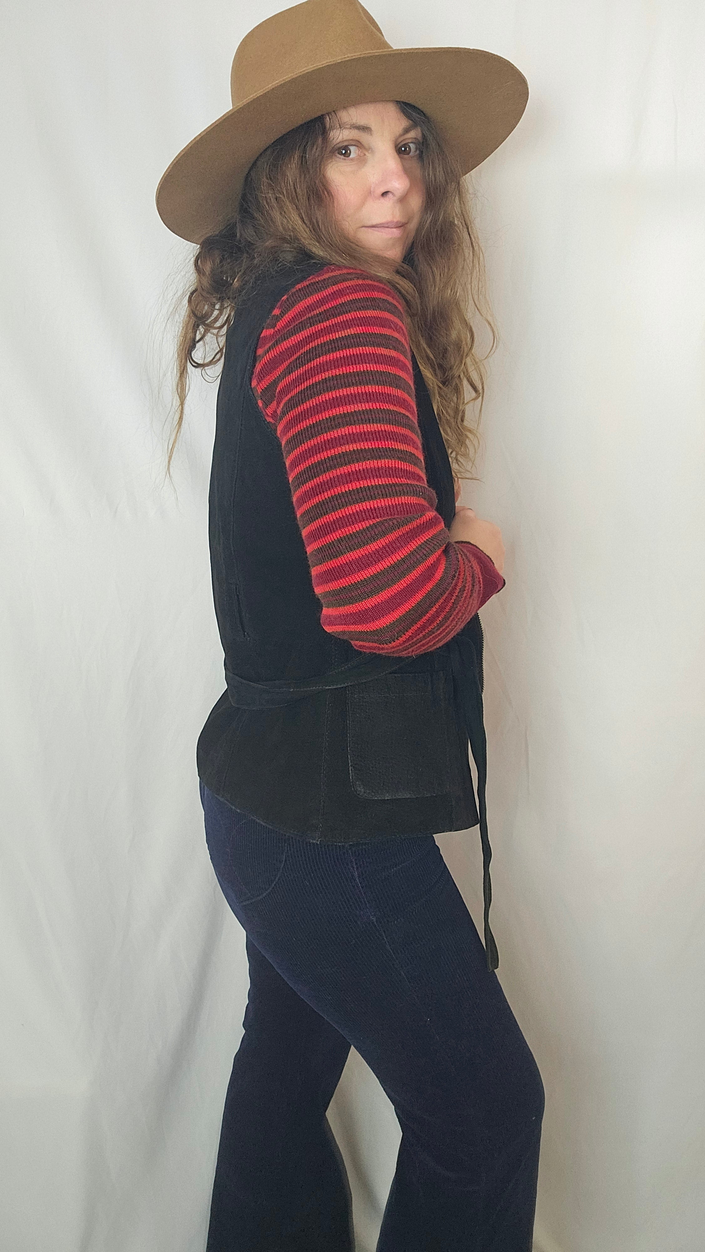 Person wearing a black coat, red striped shirt, and brown hat on a white background