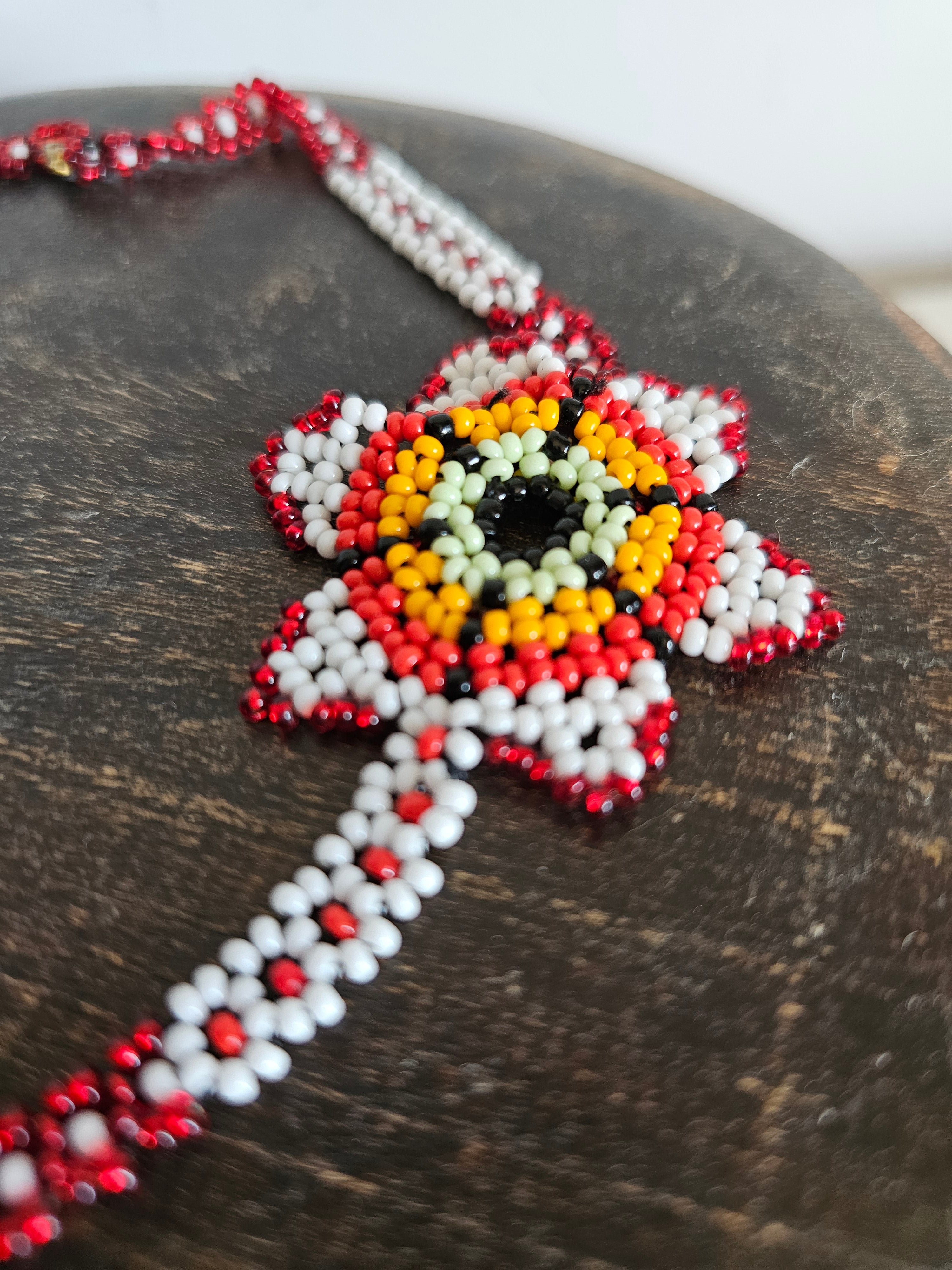 Beaded necklace with red, white, and yellow pattern on a wooden surface