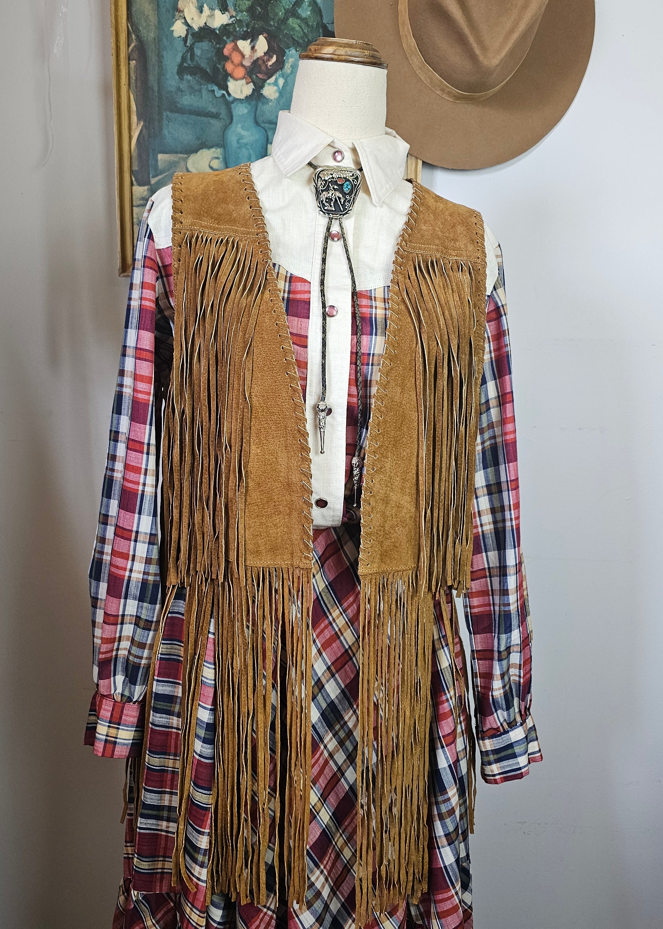 Mannequin wearing a brown fringe jacket over plaid shirt with a hat on a white background