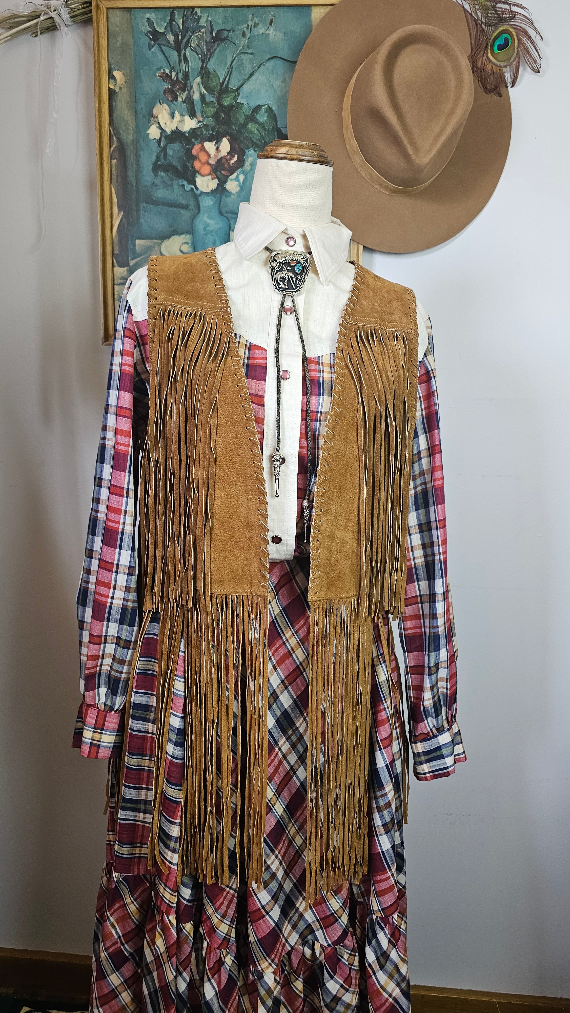 Mannequin wearing a brown fringe jacket over plaid shirt with a hat on a white background