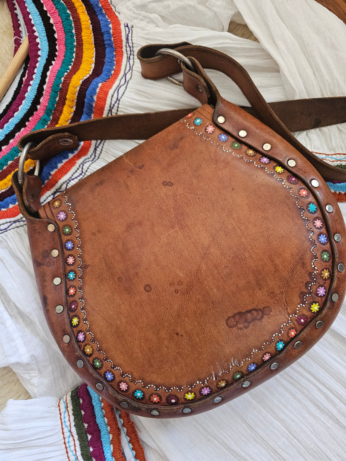 Brown leather bag with colorful studs on a striped fabric background