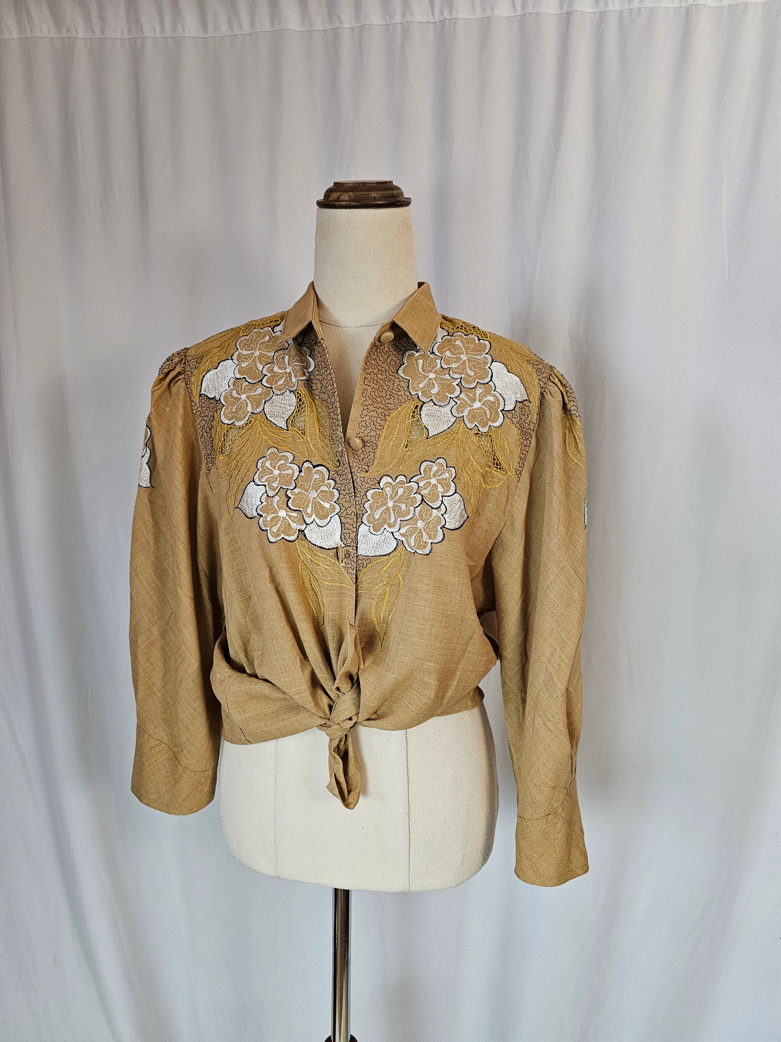 Beige traditional garment with floral embroidery on a mannequin against a plain background