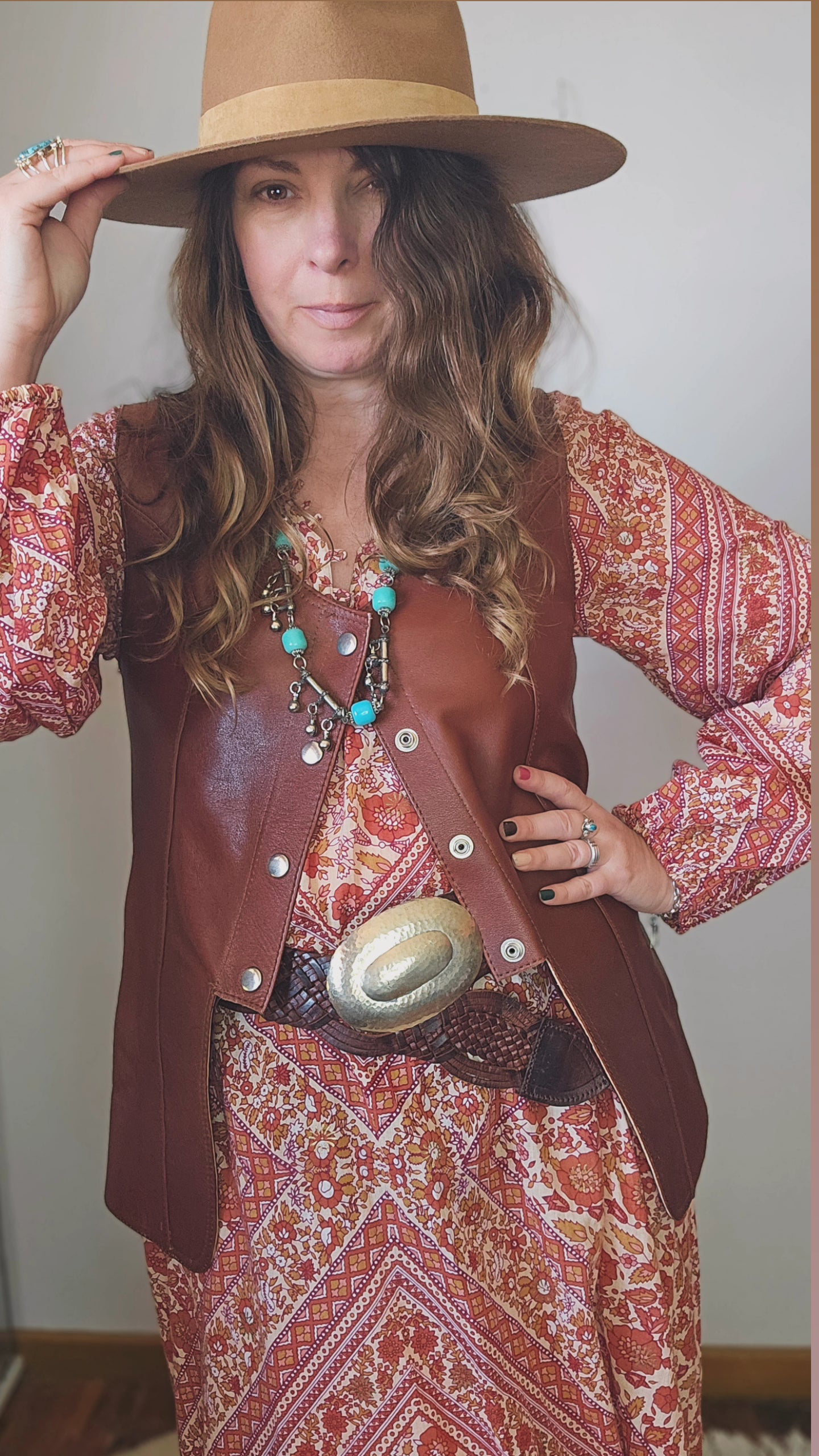 Woman wearing a brown hat, patterned dress, and leather vest with a belt buckle.