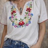 Woman wearing a white blouse with colorful floral embroidery and blue jeans.