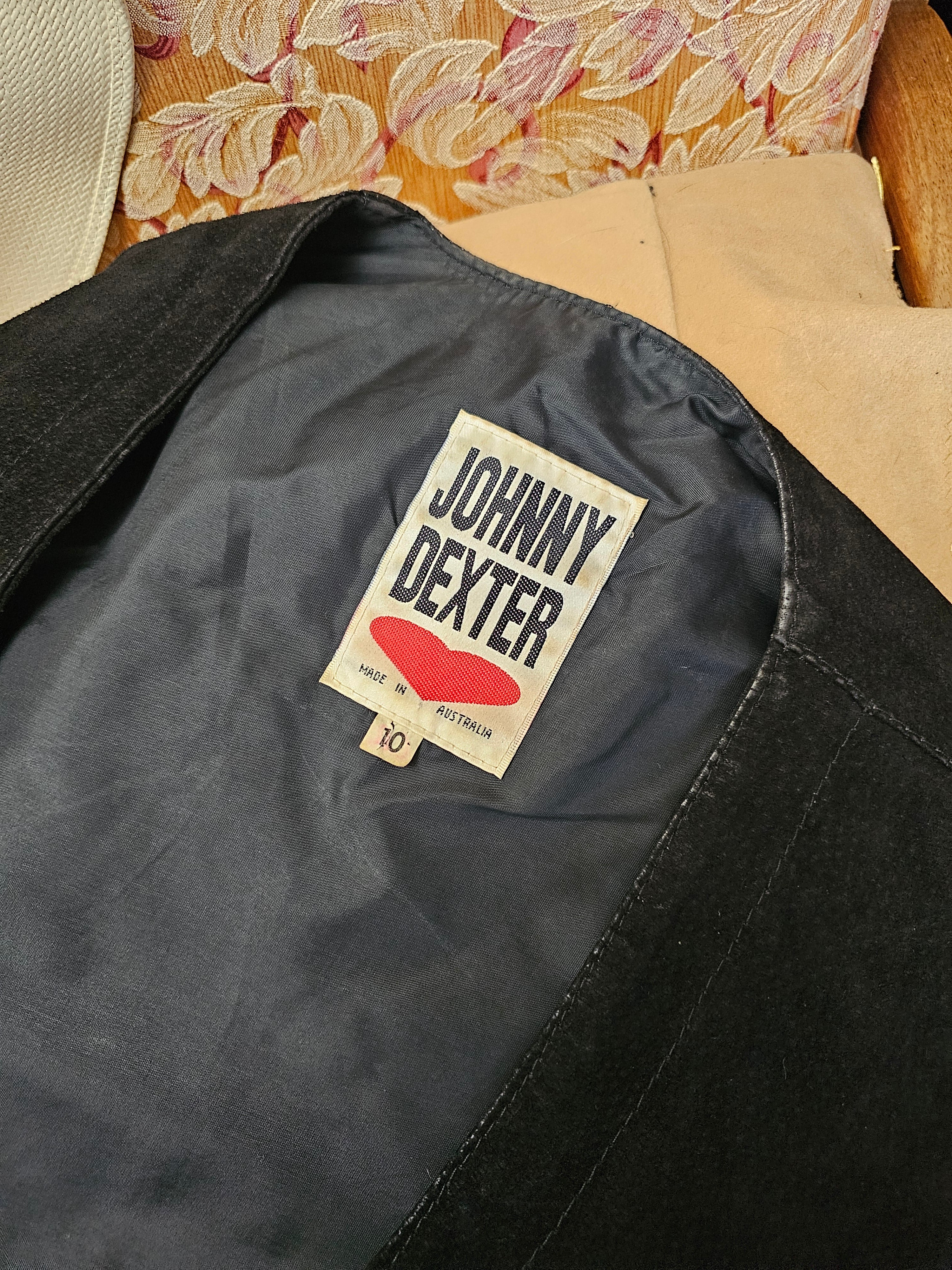 Close-up of a Johnny Dexter label on a black garment with a floral pattern in the background.