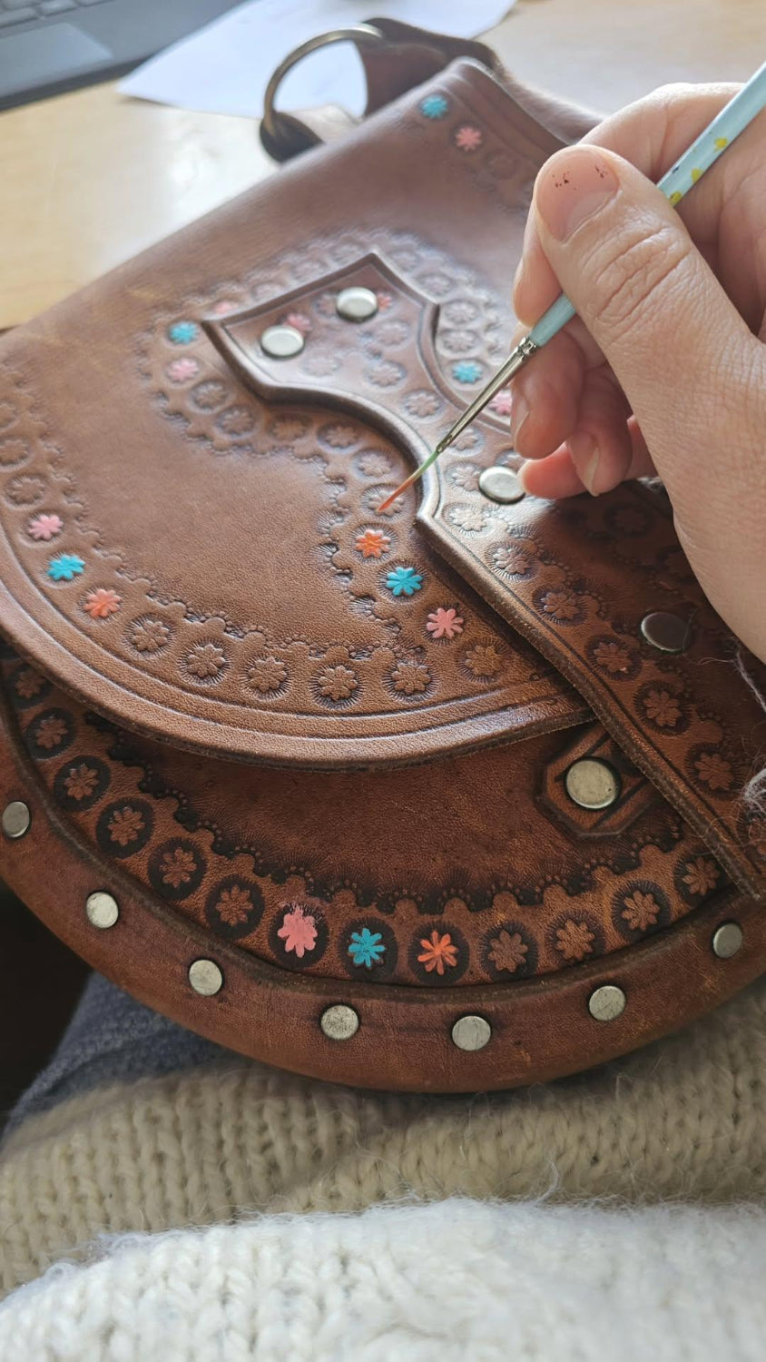 Person working on a brown leather saddle with decorative studs and patterns.