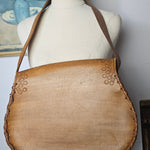 Mannequin wearing a brown leather handbag with floral patterns on a white background