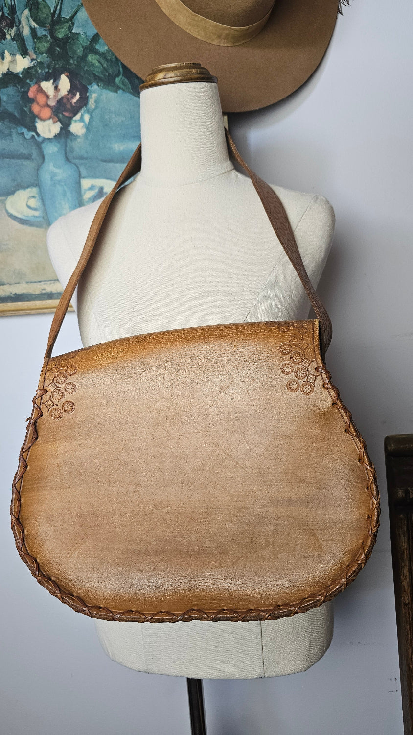 Mannequin wearing a brown leather handbag with floral patterns on a white background