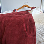 Close-up of a maroon corduroy pants on a hanger against a neutral background
