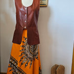 Mannequin wearing a brown leather jacket and orange dress with black embroidery on a white background.