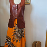 Mannequin wearing a brown leather jacket and orange dress with black embroidery on a white background.