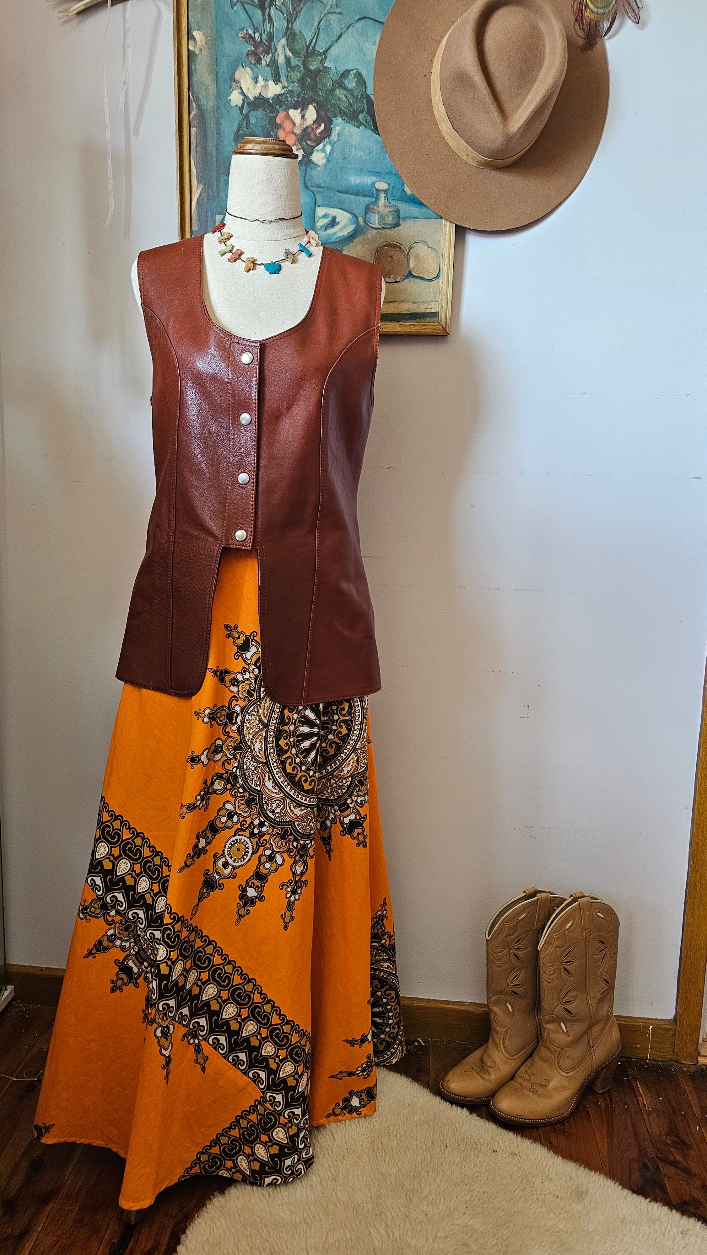 Mannequin wearing a brown leather jacket and orange dress with black embroidery on a white background.