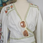 Mannequin wearing a white dress with floral embroidery on a plain background