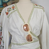 Mannequin wearing a white dress with floral embroidery on a plain background