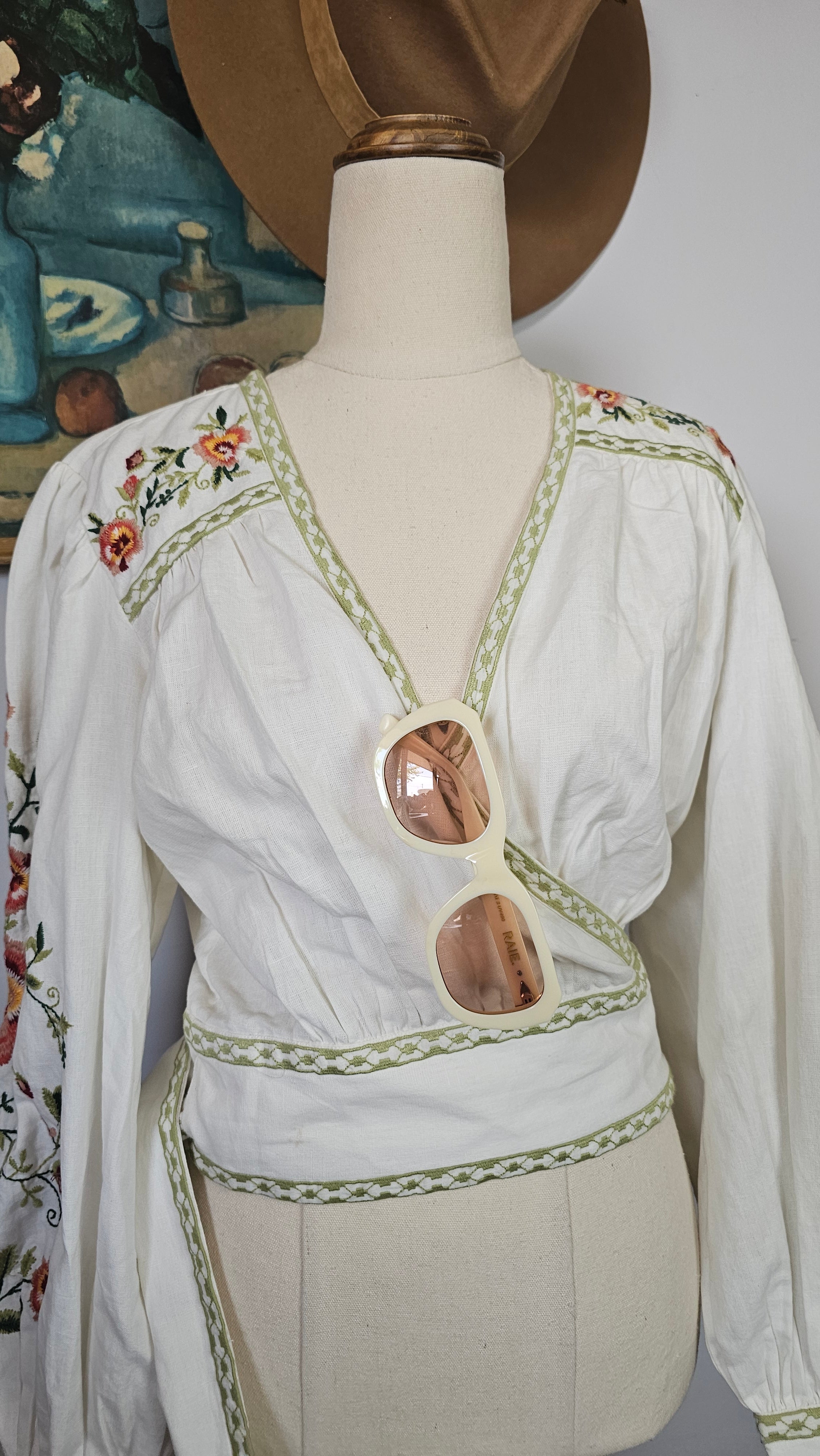 Mannequin wearing a white dress with floral embroidery on a plain background