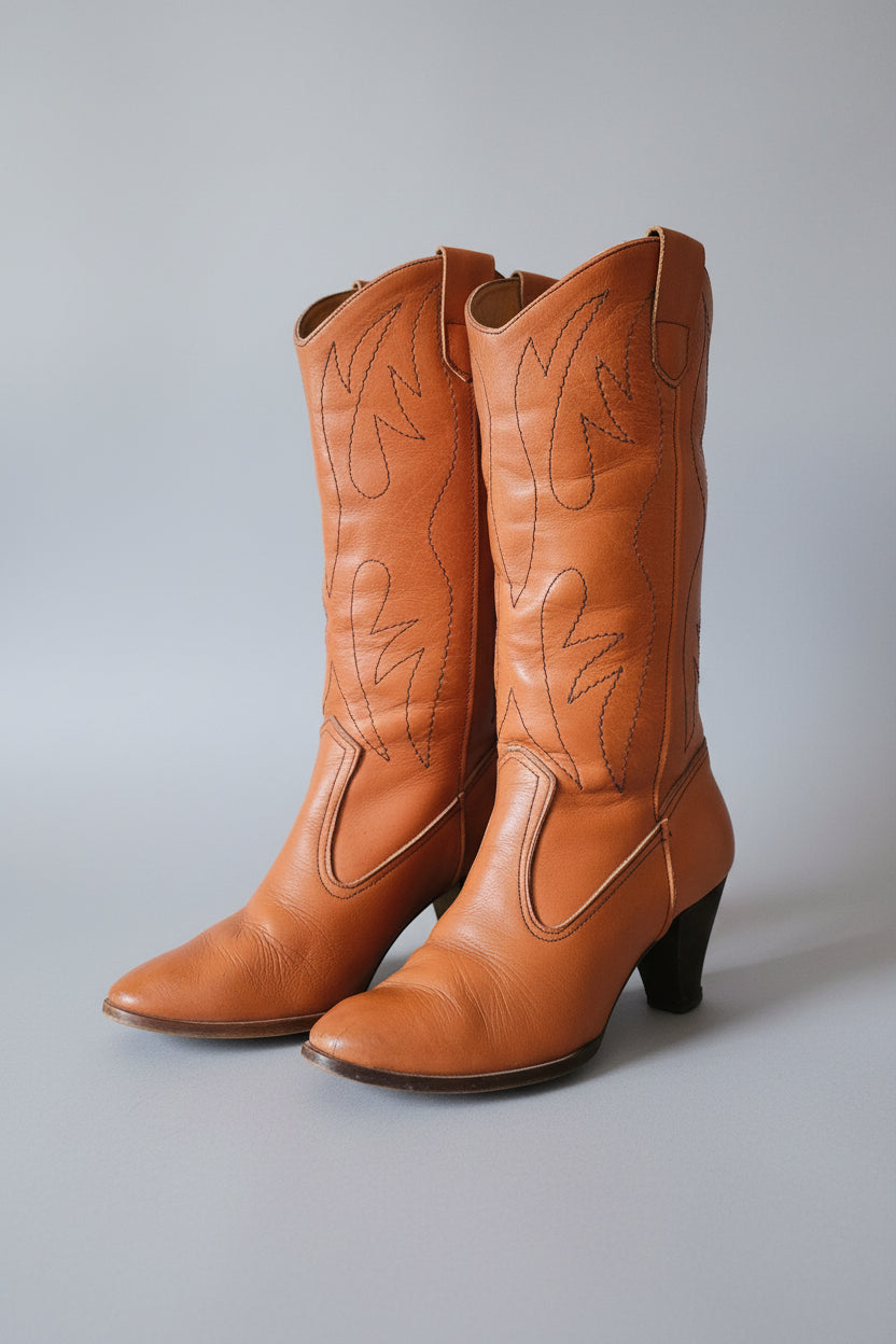 Pair of brown leather cowboy boots on a wooden surface.