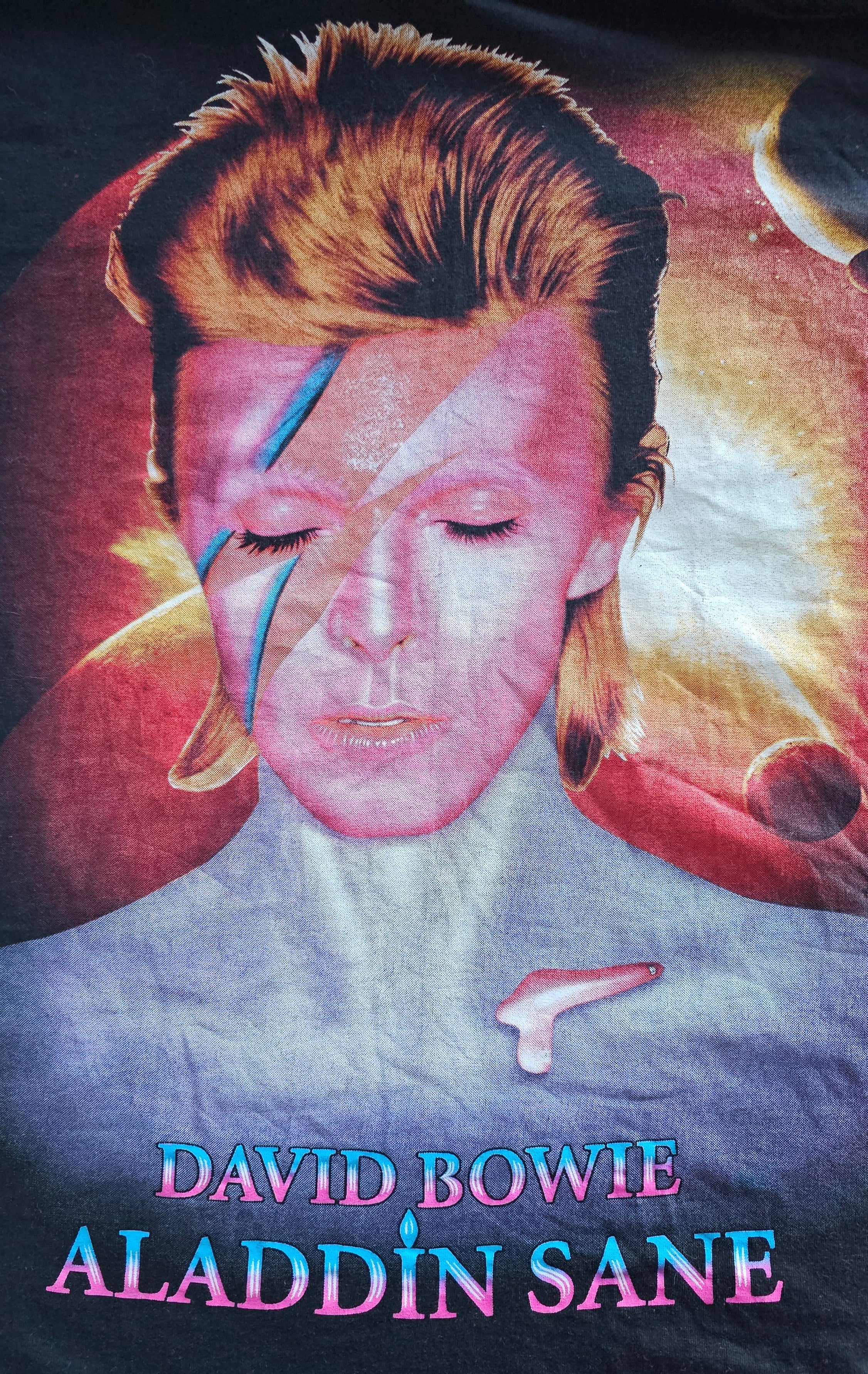 Close-up of a David Bowie 'Aladdin Sane' graphic t-shirt featuring the album cover art and title text on a dark background.
