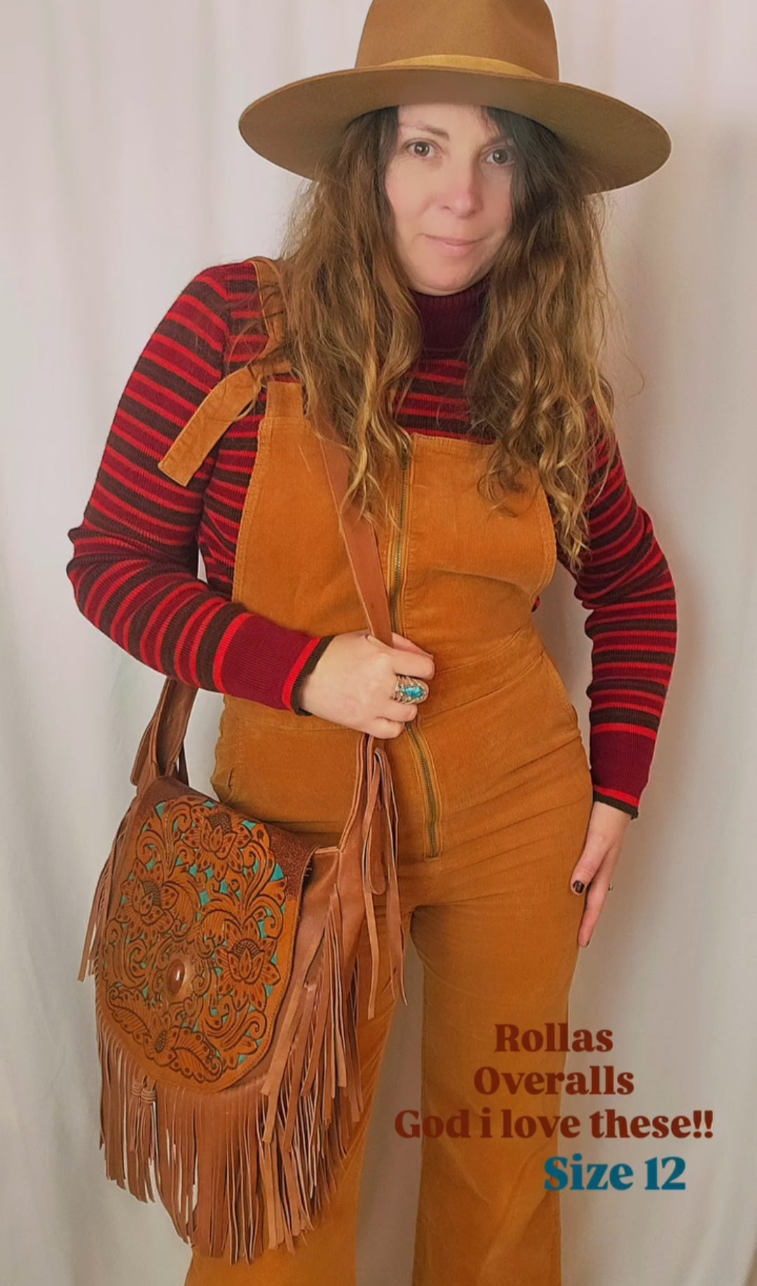 Person wearing mustard yellow overalls with a red and black striped shirt, holding a brown leather bag.