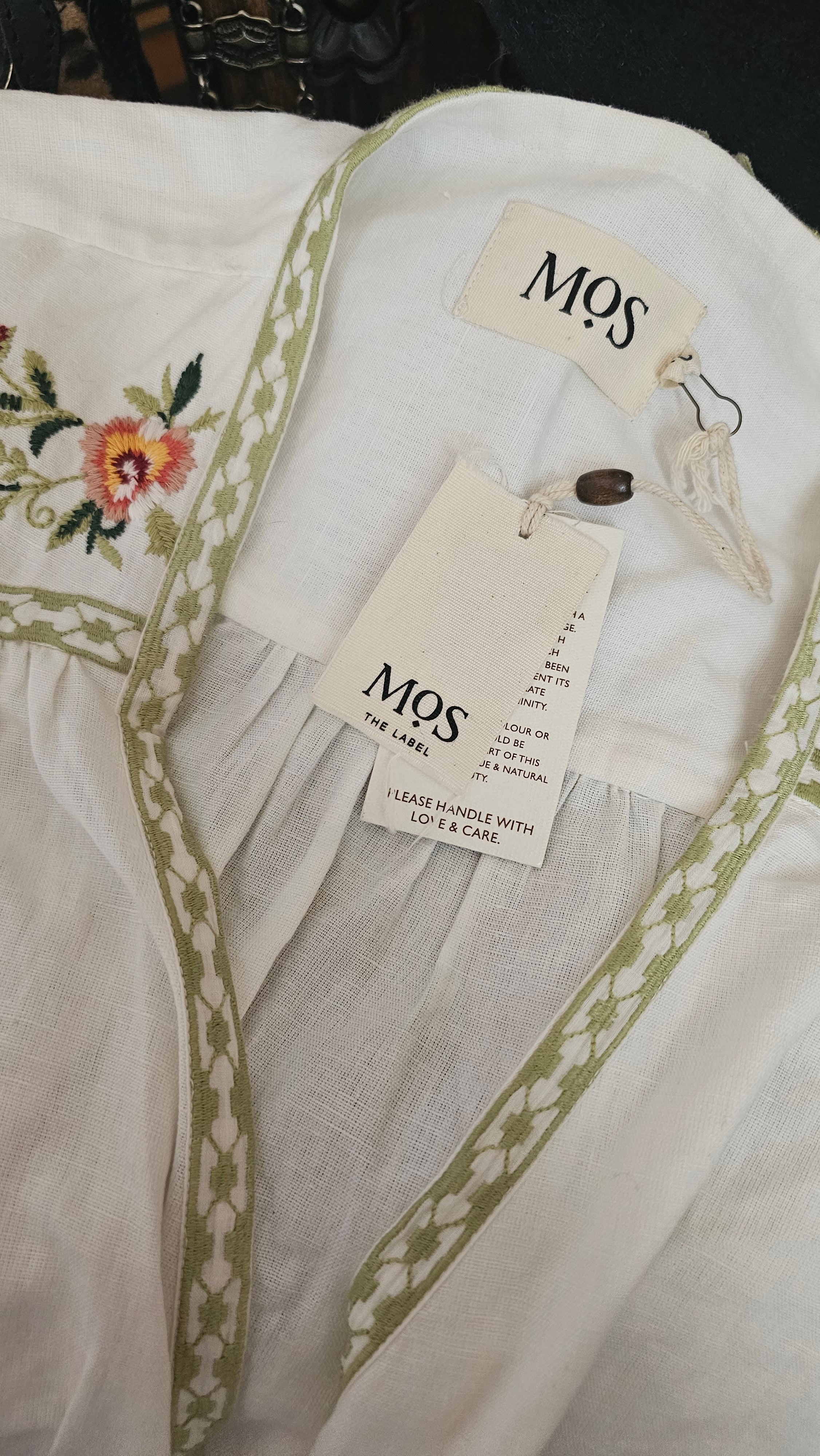 White fabric with green embroidery and floral design, featuring 'MOS' tags.