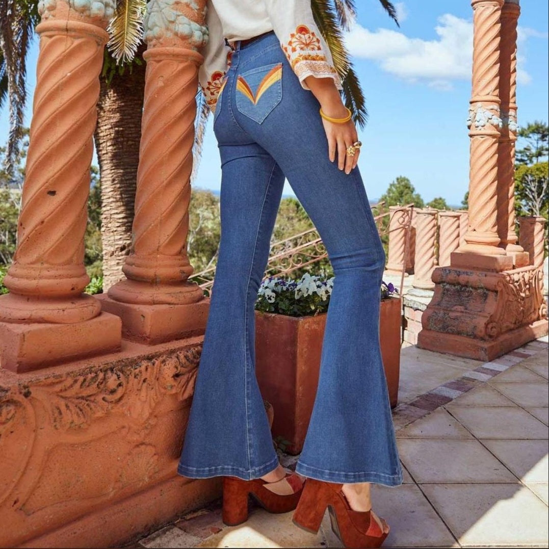 Person wearing blue flared jeans standing in front of decorative columns with a scenic background.
