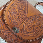 Brown leather bag with intricate embossed design on a light background