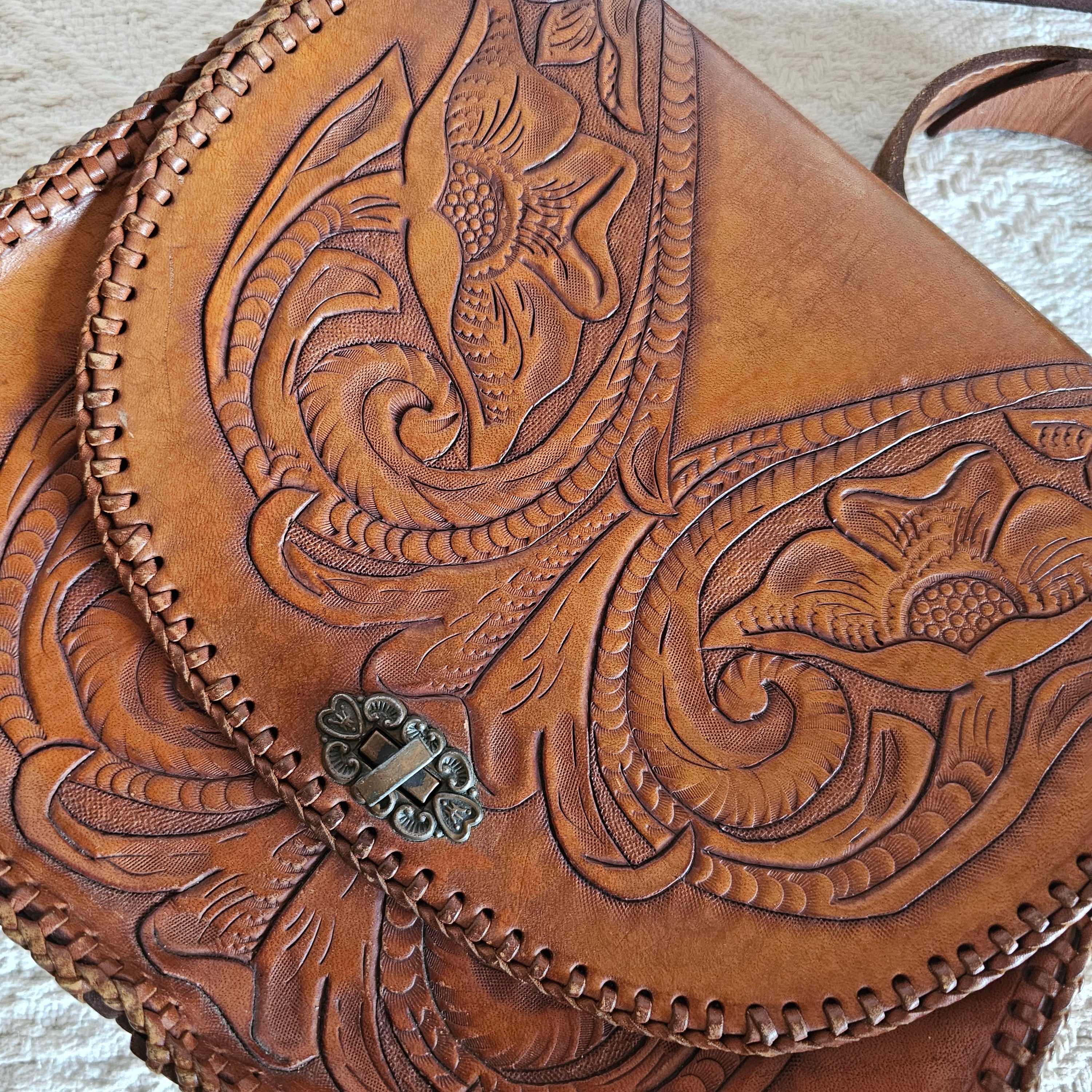 Brown leather bag with intricate embossed design on a light background