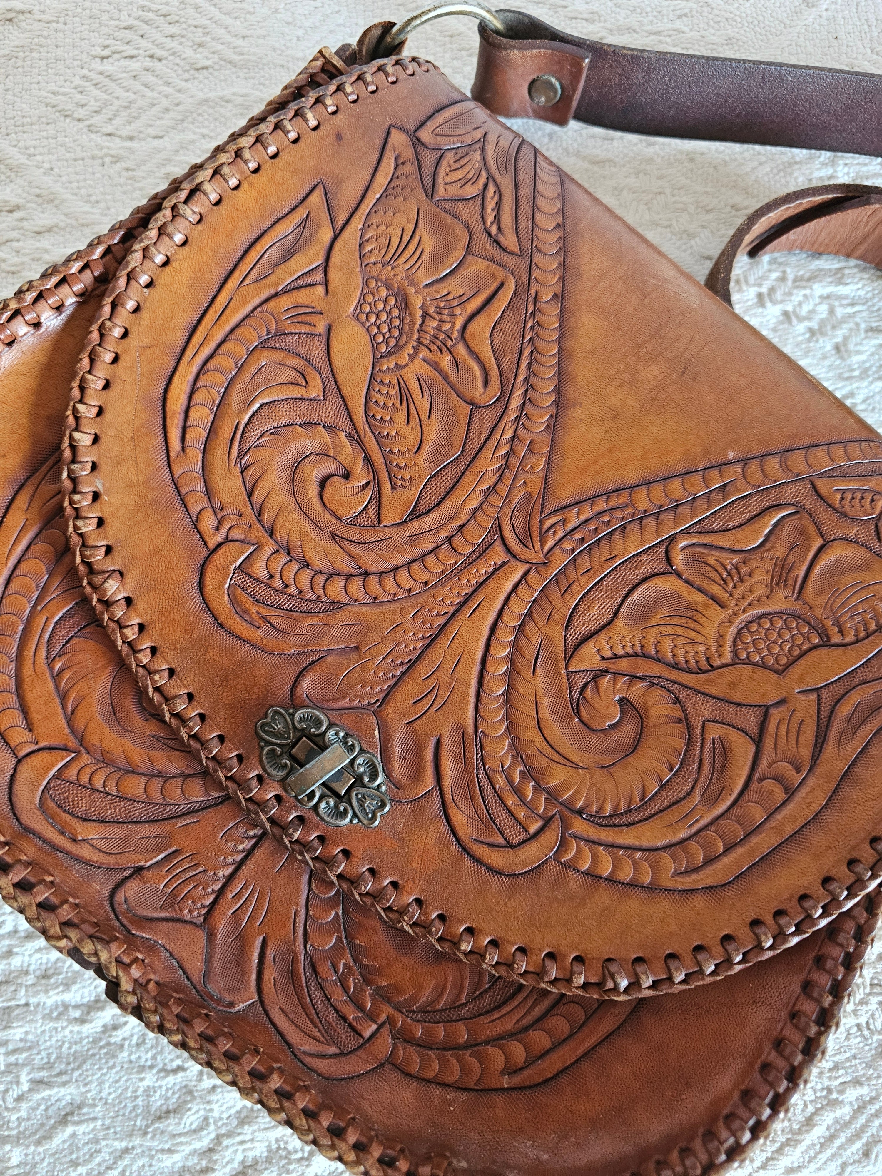Brown leather bag with intricate embossed design on a light background