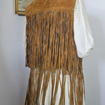 Close-up of a fringed leather bag with a hat and book in the background