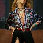 Person wearing a colorful patterned shirt and black pants with a high slit, standing against a dark background.