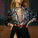 Person wearing a colorful patterned shirt and black pants with a high slit, standing against a dark background.