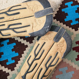Pair of tan cowboy boots with black tread pattern on a patterned rug