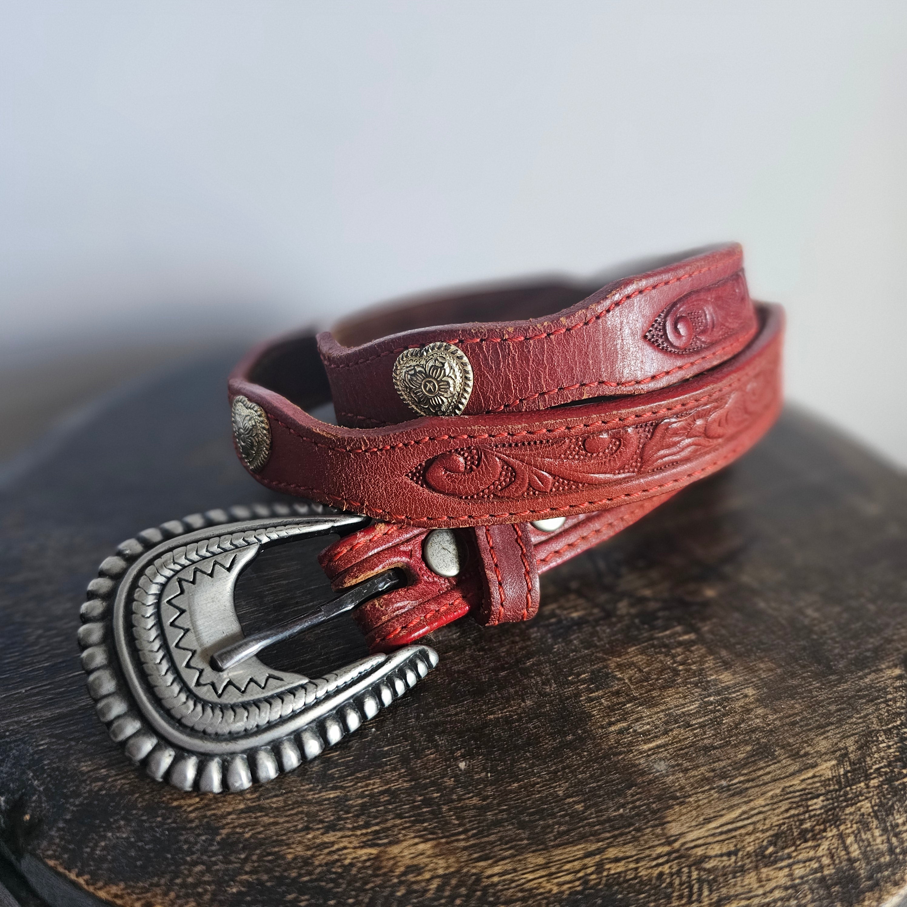 Red leather belt with silver buckle on a wooden surface
