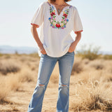 White blouse with floral embroidery on a mannequin against a neutral background